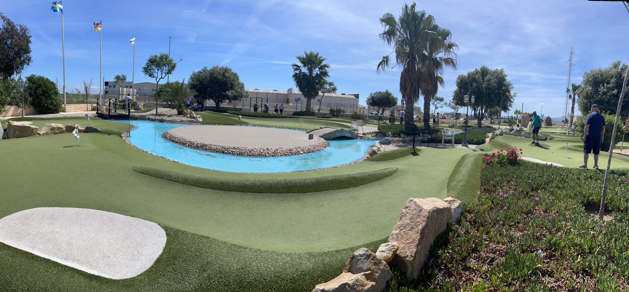 Panoramic view of the Golf Delux adventure golf course with lake, palms and flags